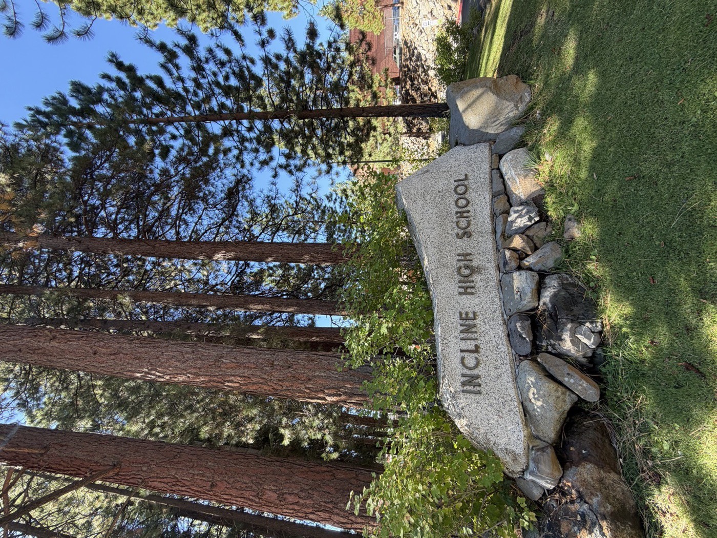 The granite Incline High School sign set among pine trees