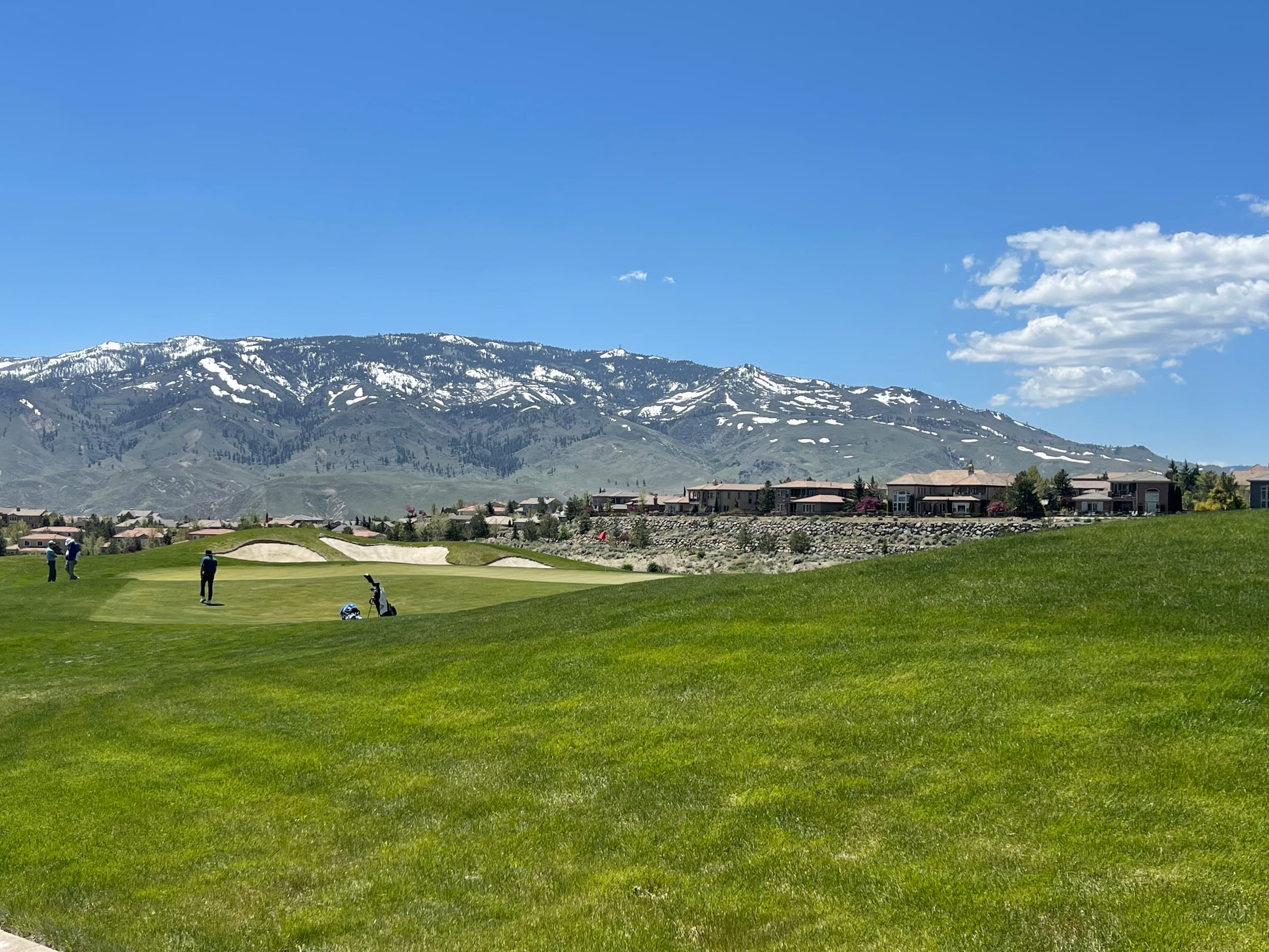Golfers on the green at Somersett Golf and Country Club, with homes behind a stone wall